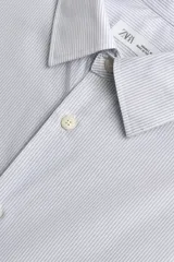 Camisa de corte regular fit confeccionada en tejido de algodón con diseño de rayas verticales finas. Presenta cuello italiano, manga larga con puños abotonados y cierre frontal mediante botonadura.