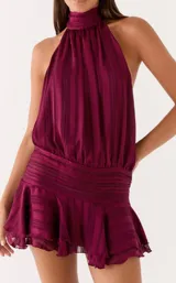 Vestido corto color bordó con escote halter fruncido, diseño sin mangas, cintura ajustada con fruncido horizontal y falda corta con volados.