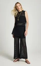 Musculosa de punto negro Le Lis Blanc, de corte recto, escote redondo, sisas amplias y tejido calado con transparencia. Presenta un diseño asimétrico con superposición frontal y detalle de anillo metálico en el lateral.