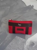 Sobre de lona color rojo con terminaciones en cuero marrón y aplique metálico de caballo en la parte frontal.