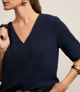 Blusa Cortelle de corte holgado confeccionada en crepé, con escote en V delantero y trasero, y mangas cortas. Presenta una tira decorativa entre los hombros en la espalda.