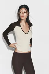 Camiseta de manga larga, corte slim fit, con cuerpo color beige claro y mangas y cuello polo en color marrón oscuro. Presenta un escote en pico bajo el cuello polo.