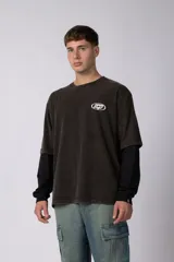 Remera de doble capa con diseño de efecto superpuesto. La capa exterior es de algodón con lavado acid wash en color gris oscuro y cuenta con un logo ovalado estampado en el pecho. La capa interior es de manga larga en color negro liso. Presenta un corte relajado y cuello redondo.