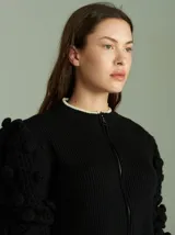 Cardigan negro de algodón con cierre frontal doble, cuello a la base y mangas tipo jamón con bordados en ochos y apliques de pompones. Presenta terminaciones acanaladas en contraste en cuello, puños y ruedo.