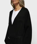 Enterito negro de piqué y sarga de Tencel lavado, con escote en V, mangas largas y corte holgado. Presenta bolsillos de parche en pecho y espalda, bolsillos laterales y cinturón doble de cordón. Tiene detalles de bordado en el pecho y un parche con borde sin rematar en la espalda.