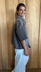 Sobrecamisa de denim soft en tono azul medio, con corte oversize, mangas cortas, cuello clásico y cierre frontal con botones metálicos. Presenta dos bolsillos frontales con solapa y un ruedo redondeado.