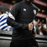Buzo negro de entrenamiento de la selección uruguaya de fútbol (AUF) con medio cierre, cuello alto, logo de la AUF en el pecho y detalles en gris en los hombros y mangas.
