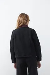 Campera de jean color negro con cuello de pana en tono marrón, cierre frontal con botones metálicos y bolsillos frontales tipo cargo.
