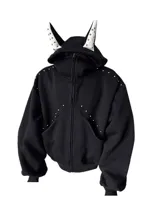Campera negra con cierre frontal, capucha con orejas decorativas blancas con tachas, y detalles de tachas metálicas en el frente y hombros. Diseño de corte regular.