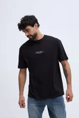Remera oversize negra de manga corta, con calce amplio y estampa gráfica en la espalda con texto en tonos azules y dorados.