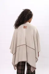 Ruana de algodón en color beige con detalles de costura decorativa en contraste color marrón. Presenta un diseño abierto con caída fluida y mangas tipo capa.