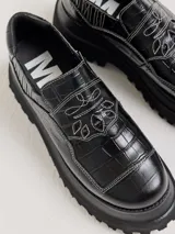 Mocasines de plataforma alta con diseño de estilo rebelde. Presentan un estampado de cuadros en tonos violeta y amarillo, confeccionados en lona con detalles en cuero. Cuentan con una suela robusta y elásticos laterales ocultos para facilitar el calce.