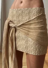 Minifalda tejida color beige dorado, con textura en zigzag y un lazo drapeado anudado en la cadera.