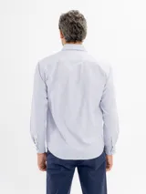 Camisa de manga larga con diseño de rayas finas, cuello con botones y bolsillo frontal. Presenta cierre de botonadura frontal y corte regular.