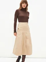 Falda midi de color beige, con diseño de tablas frontales y cierre lateral con botones decorativos. Presenta un corte estructurado y tiro alto.
