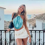 Top halter de color celeste/turquesa, con efecto drapeado y un accesorio tipo concha marina como broche central. El diseño es holgado y se ajusta en la espalda.