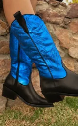 Bota texana de cuero vacuno color negro con caña alta azul con diseño bordado. Tiene cierre lateral, taco de madera con folia de cuero y horma de punta fina.