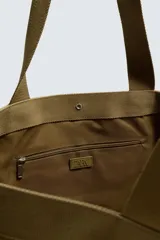 Bolso tipo shopper de gran capacidad, confeccionado en tejido con textura de pana. Cuenta con dos asas de mano resistentes, un bolsillo frontal plano y cierre principal mediante botón a presión. El interior incluye un bolsillo con cierre de cremallera.