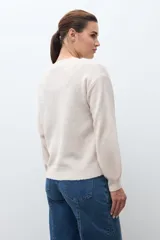 Sweater de punto en color beige melange, con cuello redondo y mangas largas. Presenta apliques de flores tejidas en relieve sobre los hombros y el pecho.