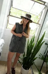 Vestido corto de jean color gris oscuro con efecto acid wash, sin mangas, con cuello camisero y cierre frontal de botones. Incluye dos bolsillos en el pecho con solapa y pespuntes decorativos.