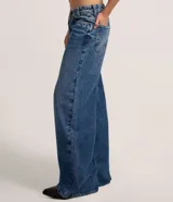 Pantalón wide leg de tiro medio confeccionado en denim de algodón. Presenta un diseño de cintura cruzada con cierre tradicional, trabillas para cinturón y bolsillos funcionales.