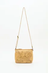 Cartera de cuero vacuno color camel con correa larga ajustable. Presenta un diseño grabado y repujado de motivos florales y arabescos, con apliques metálicos circulares en tonos plateados y dorados.