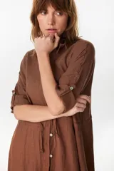 Vestido camisero largo de lino italiano color celeste, de corte relajado, con mangas caídas, jareta ajustable en la cintura, cierre frontal de botones y bajo con volado fruncido.