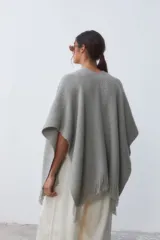 Ruana gris de tejido texturado con flecos en el borde inferior y pequeño aplique de cuero en el frente.