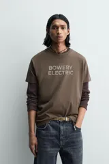 Camiseta de manga corta y cuello redondo, color marrón oscuro, con estampado frontal que dice "BOWERY ELECTRIC" en tipografía desgastada.