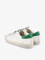 Zapatillas urbanas Golden Goose modelo Super-Star, de cuero blanco con detalles en verde en el talón y estrella en gris.