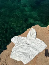 Buzo canguro con capucha, color blanco con estampado de camuflaje en tonos grises. Estampado en la espalda con el logo de la marca y nombres de ciudades.