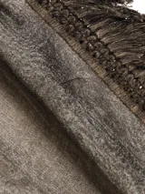 Pañuelo fino de tejido ligero, color gris, con flecos largos y densos en los bordes laterales y flecos más cortos en los bordes superiores e inferiores.