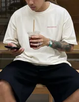 Remera oversize de algodón color crema, con cuello redondo y manga corta. Presenta un estampado pequeño en el pecho con la frase "BOHEMIAN DSG" en color rosado.