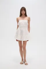 Vestido corto de algodón color blanco, con breteles finos tipo lencero, escote recto con detalle de volado y cintura con elástico fruncido. La falda presenta un diseño holgado con volado en el ruedo.