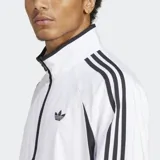 Campera deportiva Adidas Adicolor Teamgeist blanca con detalles en negro, cierre frontal, cuello alto, bolsillos laterales y las tres tiras características de la marca en las mangas.
