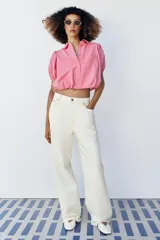 Camisa corta de cuello solapa y manga corta abullonada acabada en elástico, color verde con estampado de cuadros vichy. Cuenta con un bolsillo de plastrón en el delantero, bajo con elástico y cierre frontal con botones.