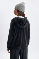 Campera de plush color negro con cierre frontal, capucha con cordones ajustables y mangas ranglan. Presenta un diseño cómodo y versátil con puños y ruedo acanalados.