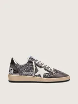 Zapatillas Golden Goose modelo Ball Star de estilo retro, con empeine y lengüeta cubiertos de glitter gris oscuro y detalles en cuero laminado. Presentan la clásica estrella lateral en cuero blanco, puntera reforzada y cordones de algodón crudo, con suela de goma desgastada.