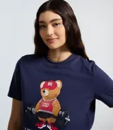 Remera de algodón color azul marino, con cuello redondo y manga corta. Presenta un estampado frontal de un oso con ropa deportiva levantando pesas, acompañado de la frase 'I Wanna Go Home'.