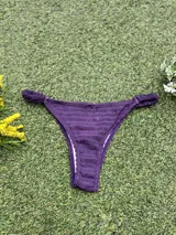 Conjunto de bikini color violeta confeccionado en tela texturada. El corpiño es de estilo top con una hebilla ovalada marrón en el centro y breteles finos. La bombacha es de corte colaless con detalle de frunces en los laterales.