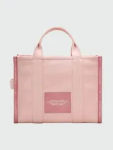 Bolso tipo tote de lona color negro con letras blancas bordadas en el frente que dicen 'THE TOTE BAG MARC JACOBS'. Cuenta con asas superiores cortas y una correa de hombro ajustable y extraíble.