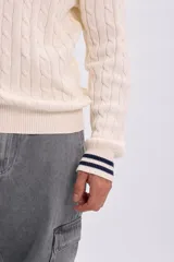 Sweater tejido de punto color crudo, con diseño trenzado y detalles de líneas azul marino en el cuello redondo y los puños.