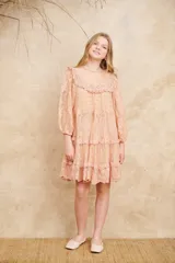 Vestido corto de encaje color durazno, con diseño de volados en capas, mangas largas abullonadas y cuello redondo con detalles bordados.