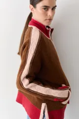 Campera de tejido de punto con cierre frontal, cuello alto y diseño color block en tonos marrón, rosa y rojo. Presenta detalles de trenzas en las mangas y puños y ruedo acanalados.