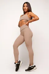 Conjunto deportivo de top y calzas color tostado, confeccionado en poliamida de alta performance con detalles de vivo contrastante. El top cuenta con breteles anchos y diseño slim, mientras que la calza presenta un diseño minimalista de tiro alto.