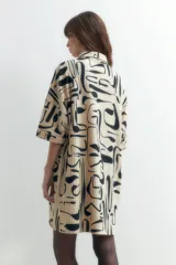 Vestido plisado color beige con estampado abstracto en negro, corte recto, cuello camisero y mangas cortas.