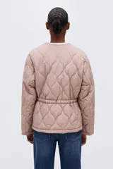 Campera acolchada de nylon guateado en color rosado, con cuello redondo, cierre frontal y cordón ajustable en la cintura con tiras colgantes. Presenta diseño acolchado con patrón de rombos, mangas largas y hombros caídos.
