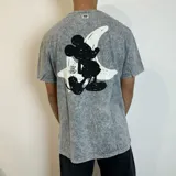 Remera de algodón con efecto lavado ácido en color gris, corte semi oversize y manga corta. Presenta un estampado gráfico en la espalda que muestra la silueta de Mickey Mouse sobre una luna blanca con el logo BY VCP.