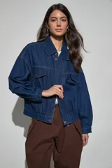 Campera de jean azul oscuro, de corte oversize, con cuello clásico, cierre frontal con cremallera y botones a presión, bolsillos frontales con solapa y mangas largas.