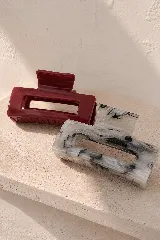 Pinza de pelo bordó de diseño rectangular con abertura central, ideal para recoger el cabello.